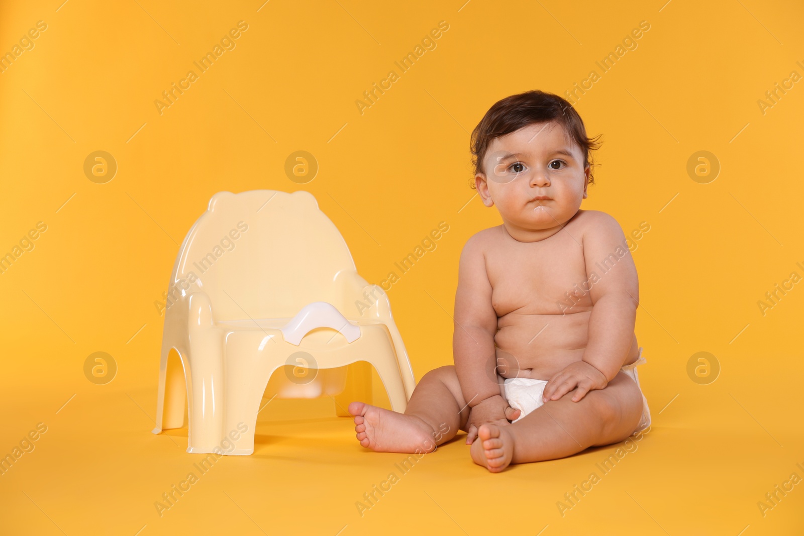 Cute little baby sitting near potty on orange background Photo of Cute little baby sitting near potty on orange background