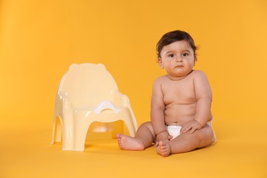 Photo of Cute little baby sitting near potty on orange background