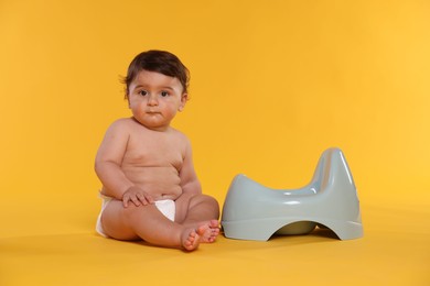 Photo of Cute little baby sitting near potty on orange background