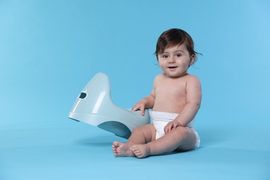Photo of Cute little baby sitting near potty on light blue background