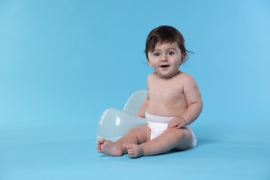 Photo of Cute little baby sitting near potty on light blue background