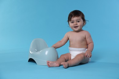 Photo of Cute little baby sitting near potty on light blue background