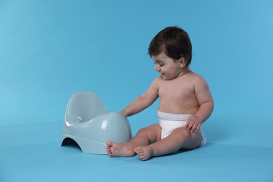 Photo of Cute little baby sitting near potty on light blue background