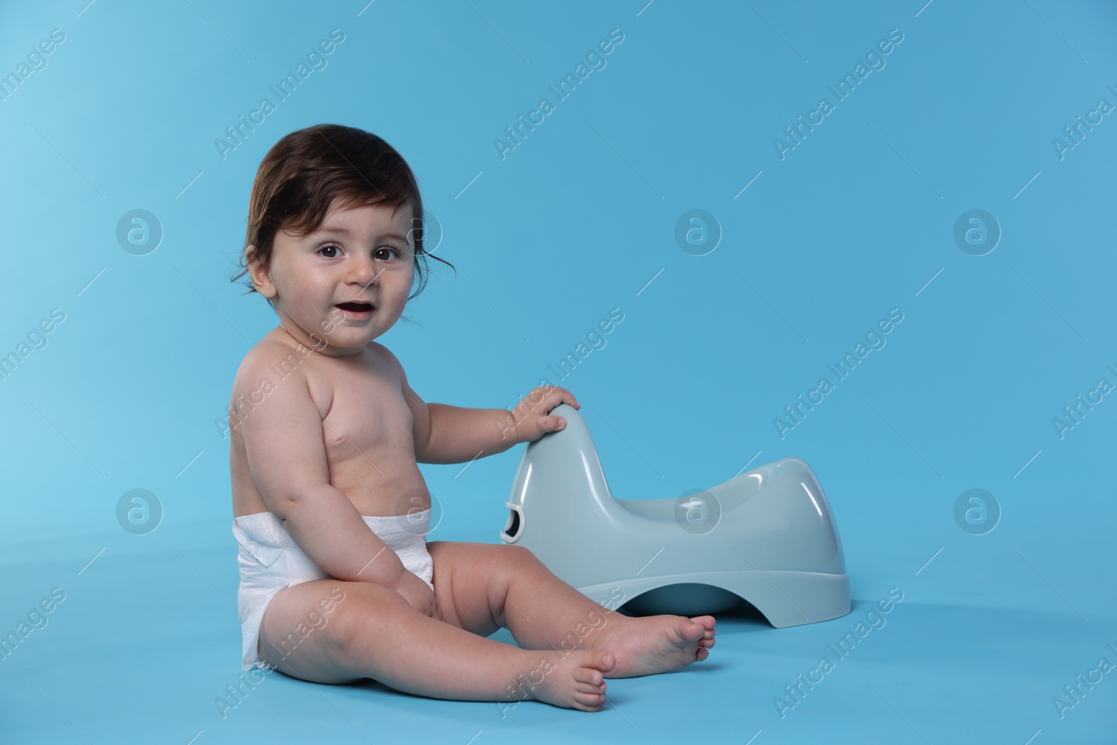 Cute little baby sitting near potty on light blue background Photo of Cute little baby sitting near potty on light blue background