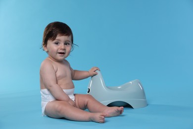Photo of Cute little baby sitting near potty on light blue background