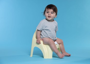 Photo of Cute little baby sitting on potty against light blue background