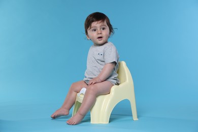 Photo of Cute little baby sitting on potty against light blue background