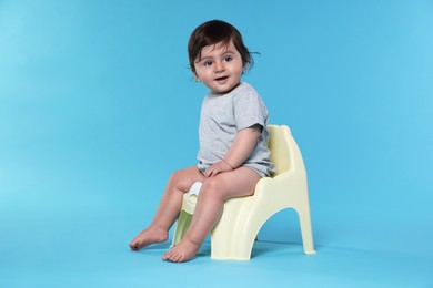 Photo of Cute little baby sitting on potty against light blue background