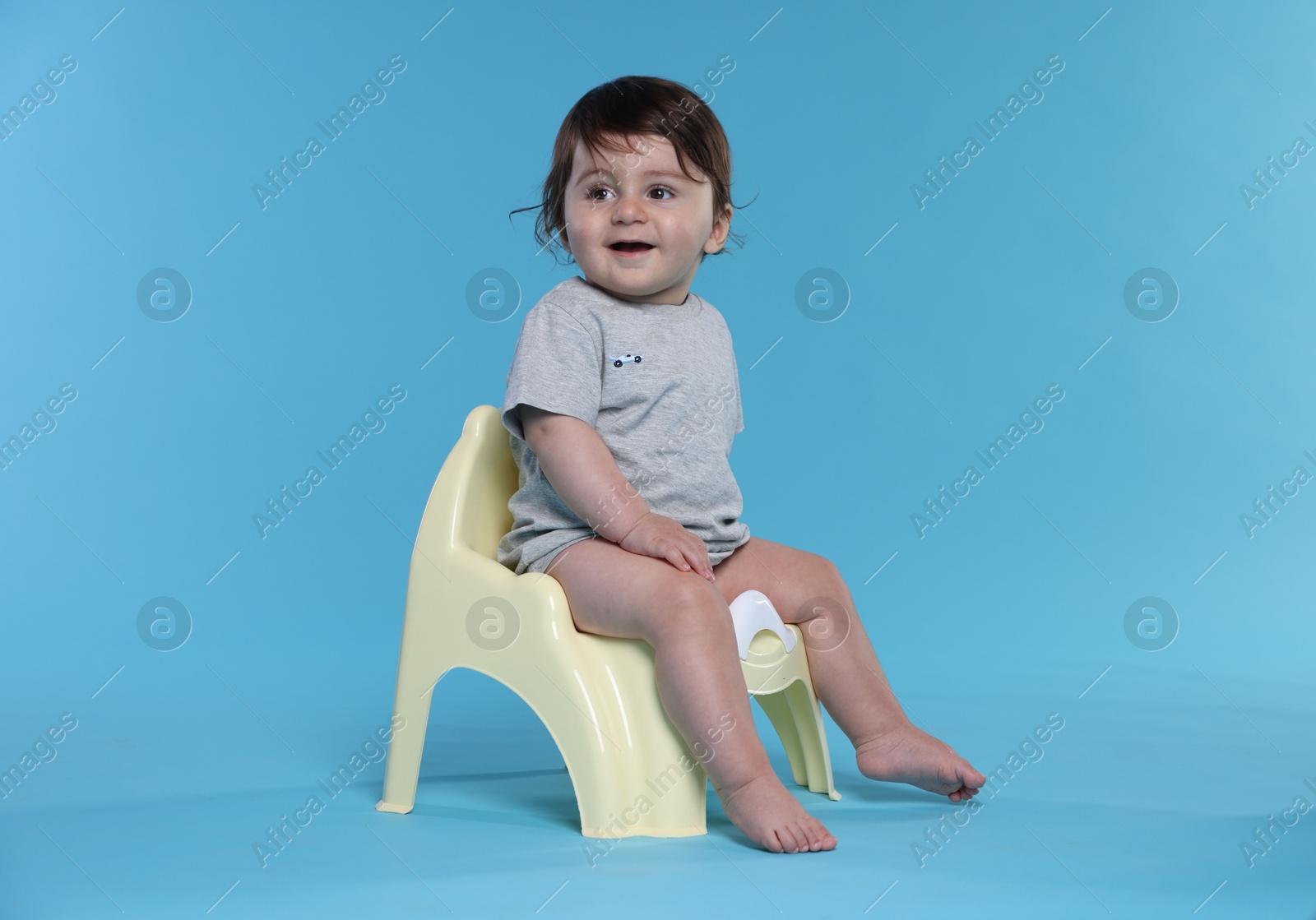 Cute little baby sitting on potty against light blue background Photo of Cute little baby sitting on potty against light blue background