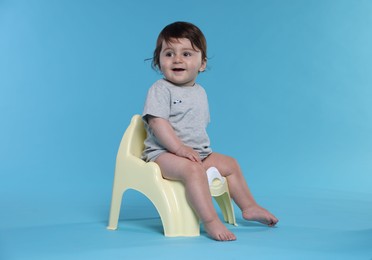 Photo of Cute little baby sitting on potty against light blue background