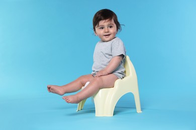 Photo of Cute little baby sitting on potty against light blue background