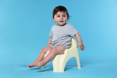 Photo of Cute little baby sitting on potty against light blue background