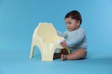 Photo of Cute little baby sitting near potty on light blue background