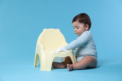 Photo of Cute little baby sitting near potty on light blue background