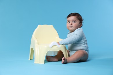 Photo of Cute little baby sitting near potty on light blue background