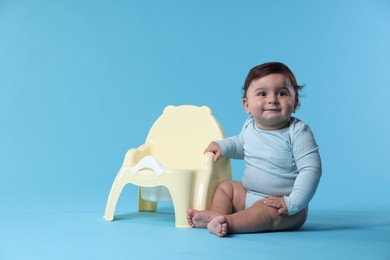 Photo of Cute little baby sitting near potty on light blue background