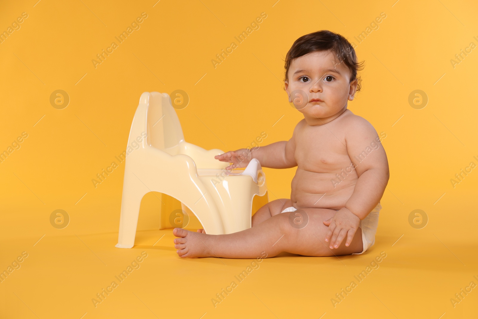 Photo of Cute little baby sitting near potty on orange background