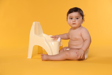Photo of Cute little baby sitting near potty on orange background