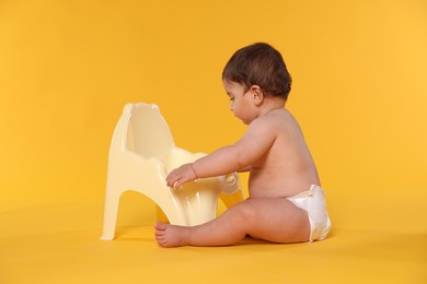 Photo of Cute little baby sitting near potty on orange background