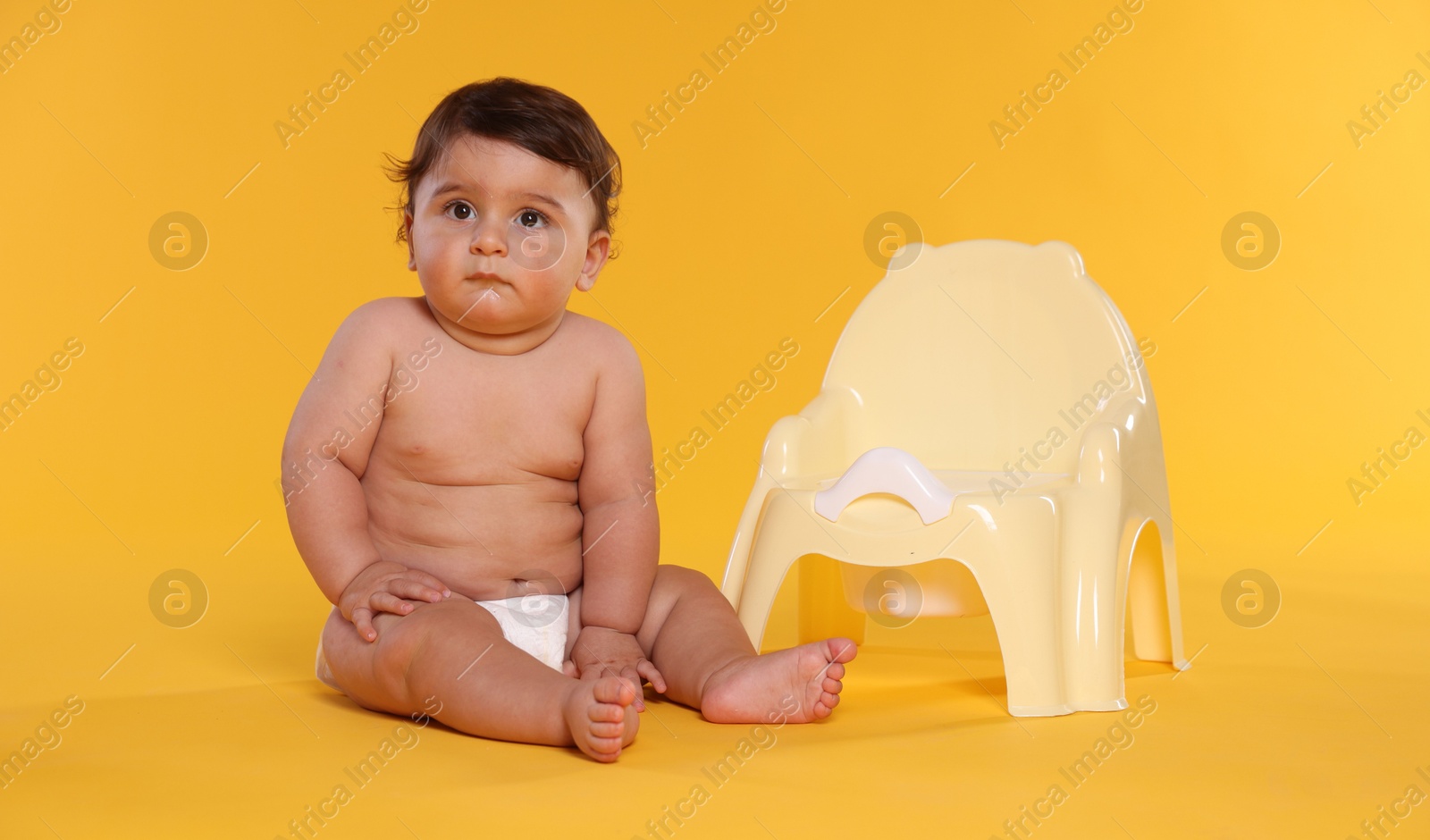 Photo of Cute little baby sitting near potty on orange background