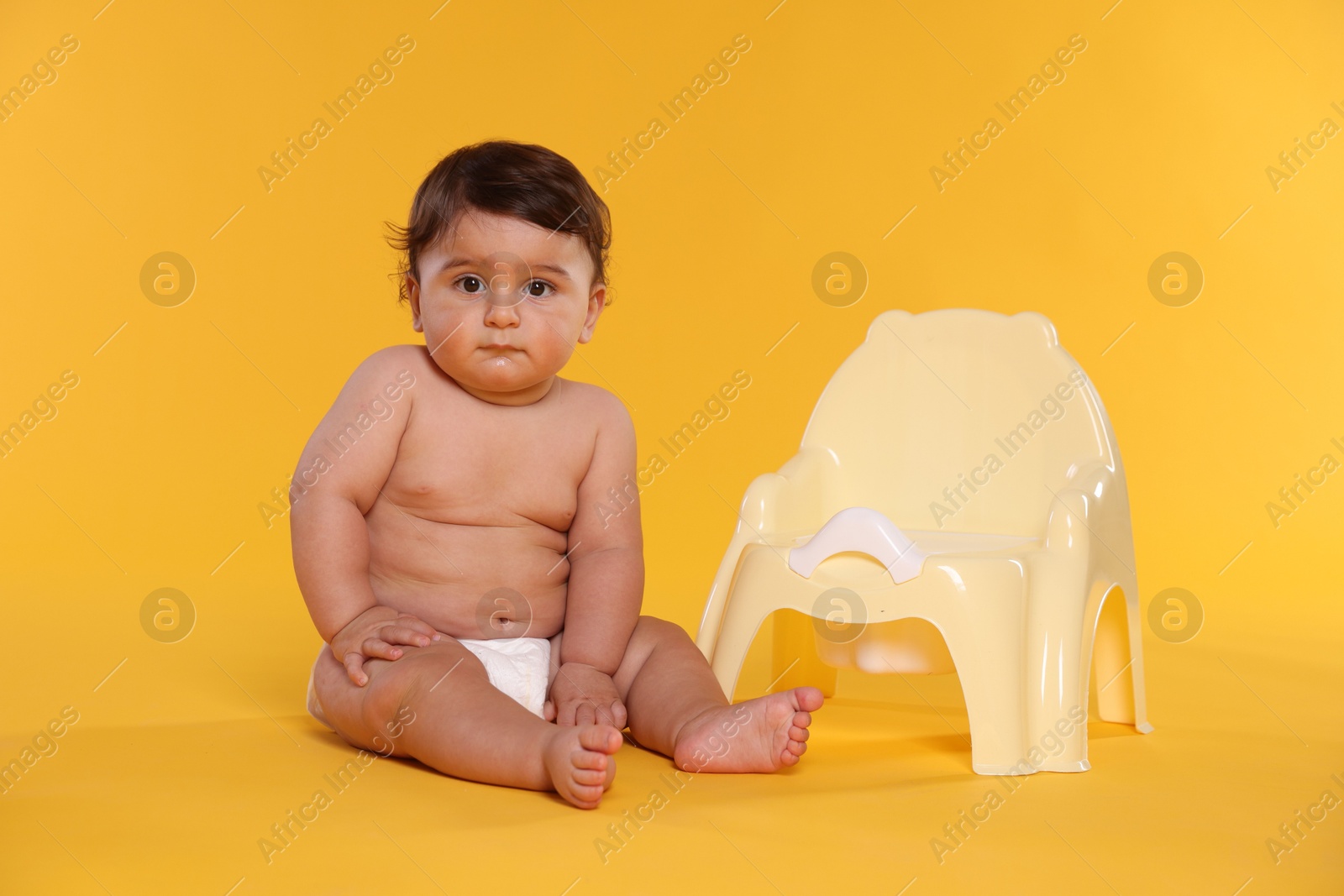 Photo of Cute little baby sitting near potty on orange background