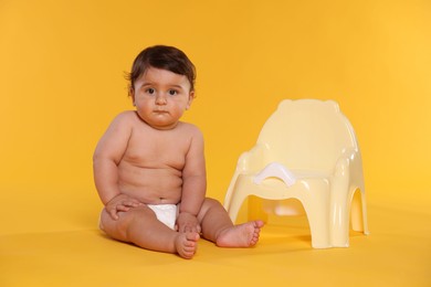 Photo of Cute little baby sitting near potty on orange background