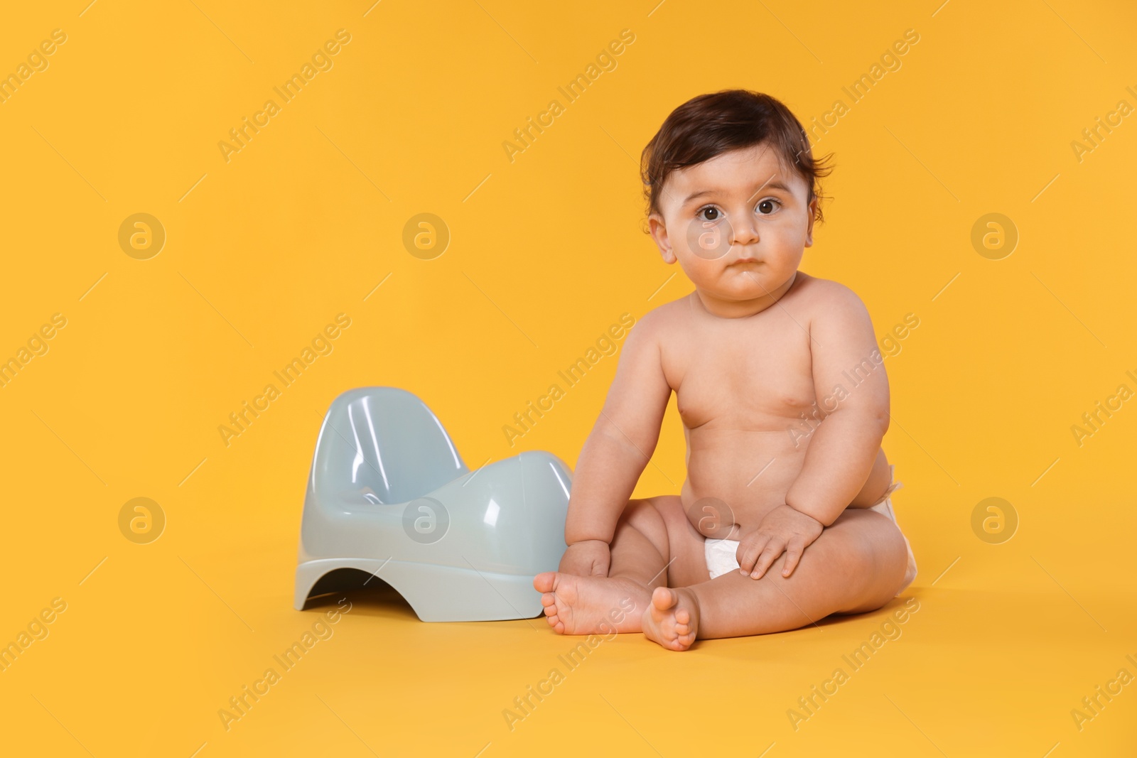 Photo of Cute little baby sitting near potty on orange background