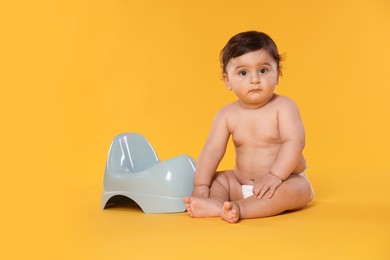 Photo of Cute little baby sitting near potty on orange background