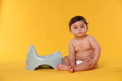 Photo of Cute little baby sitting near potty on orange background