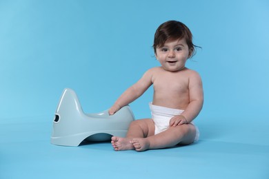 Photo of Cute little baby sitting near potty on light blue background