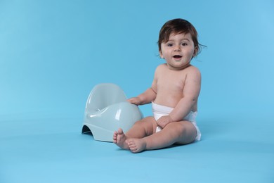 Photo of Cute little baby sitting near potty on light blue background