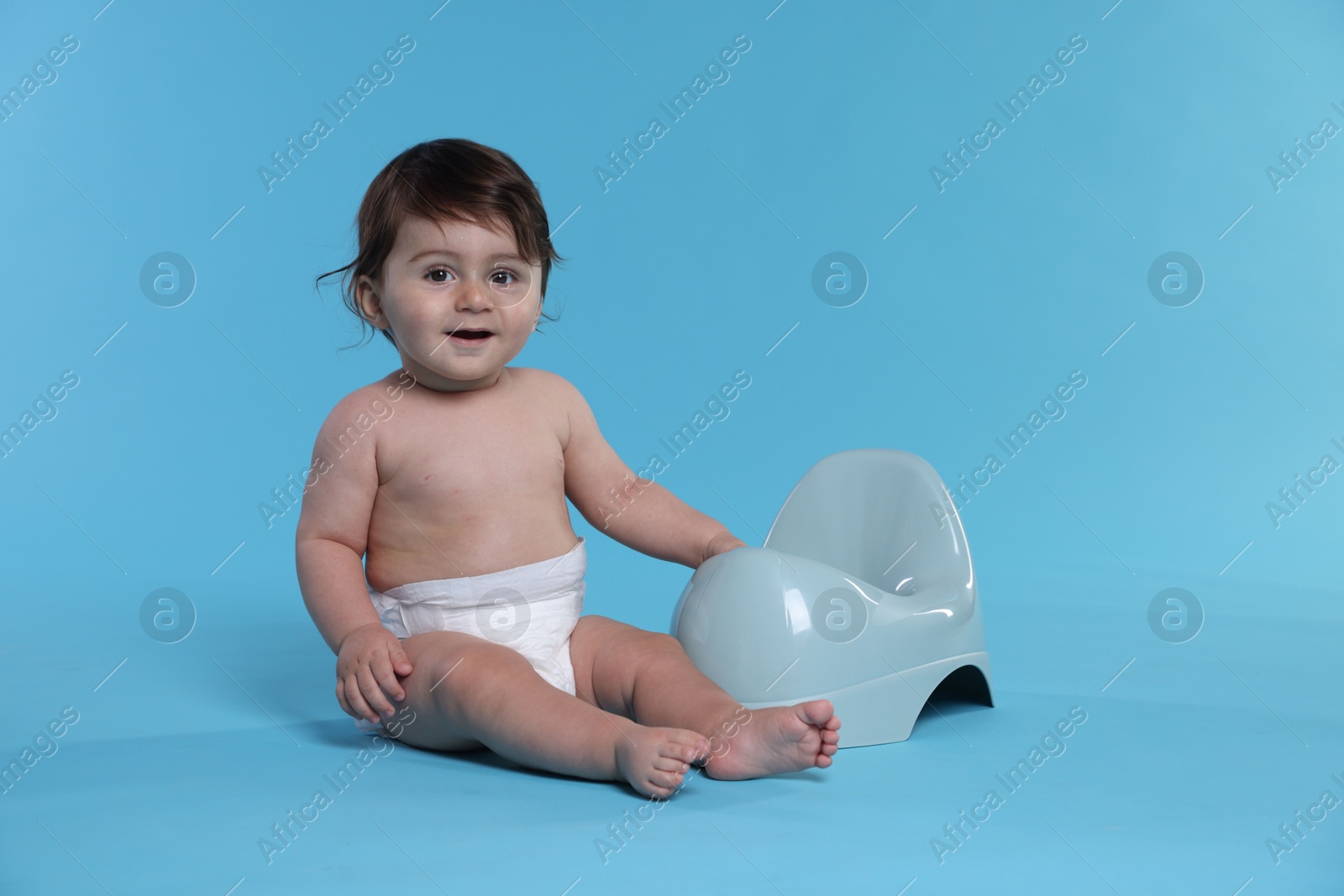 Photo of Cute little baby sitting near potty on light blue background