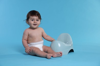 Photo of Cute little baby sitting near potty on light blue background