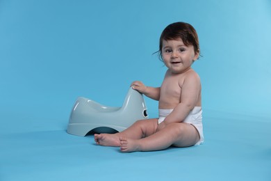 Photo of Cute little baby sitting near potty on light blue background