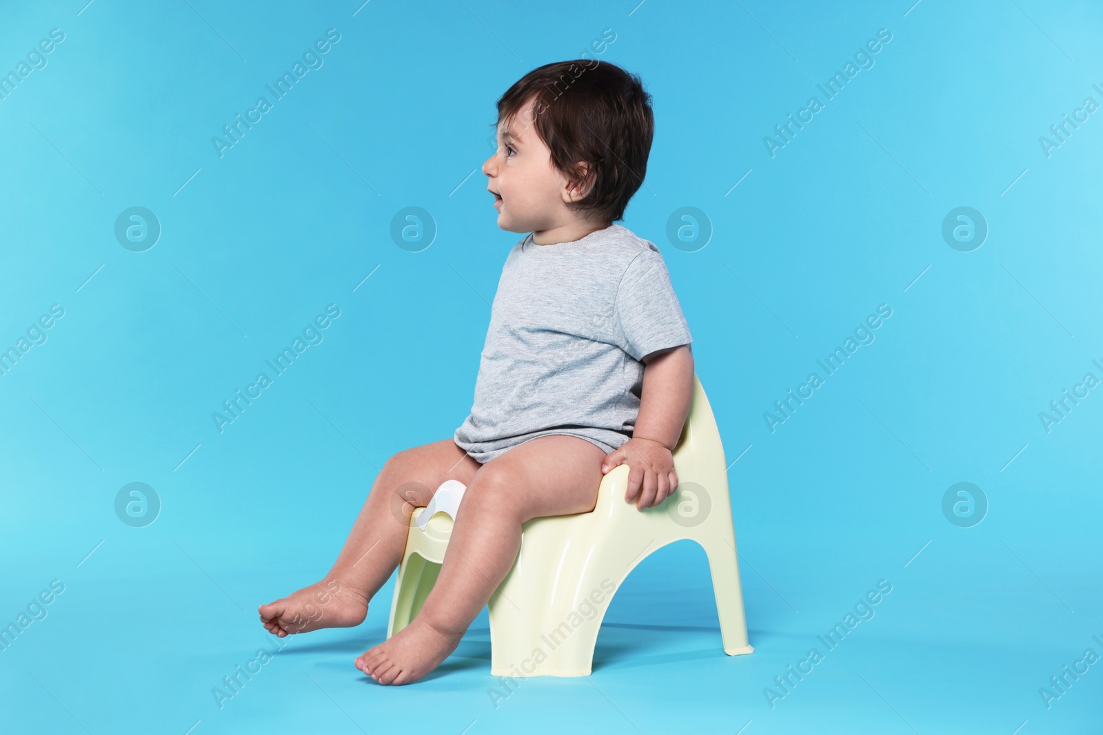 Photo of Cute little baby sitting on potty against light blue background