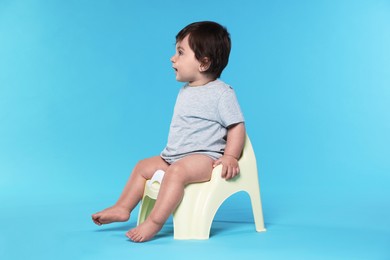 Photo of Cute little baby sitting on potty against light blue background