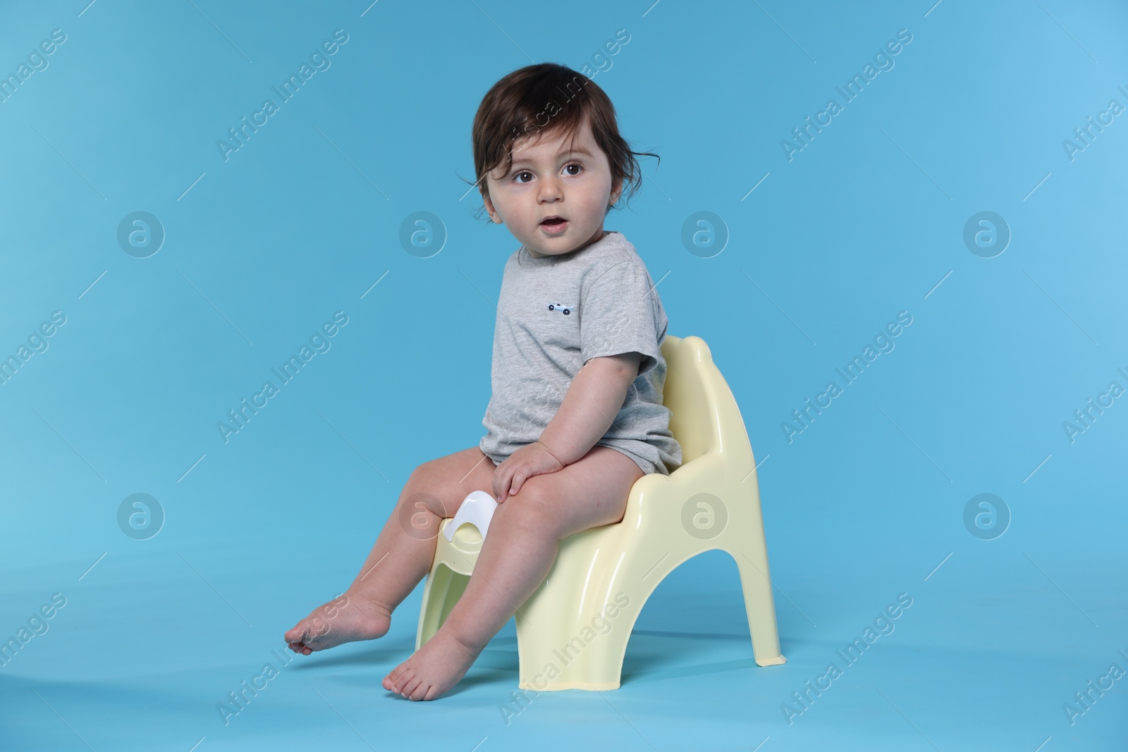 Photo of Cute little baby sitting on potty against light blue background