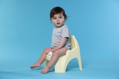 Photo of Cute little baby sitting on potty against light blue background