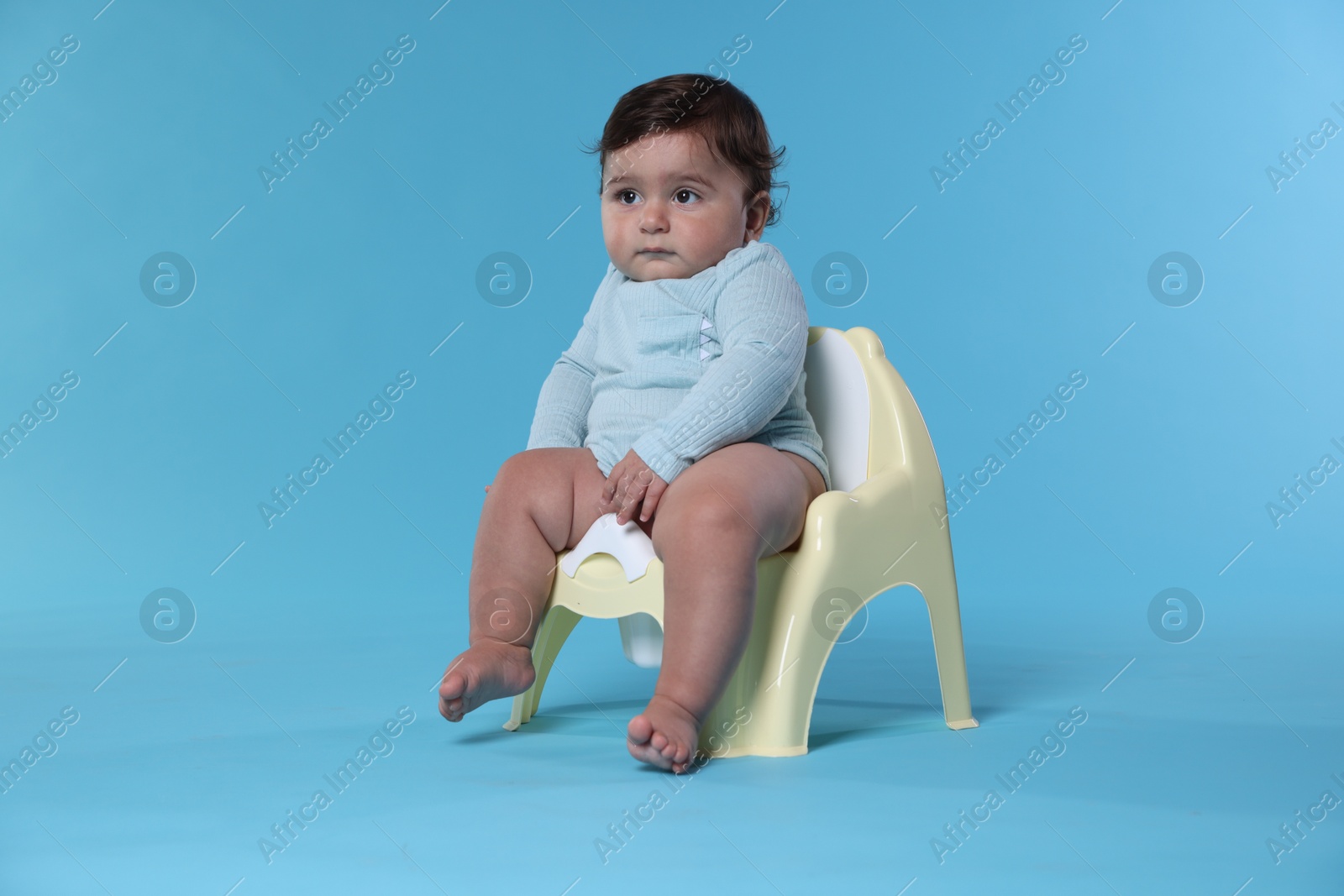 Photo of Cute little baby sitting on potty against light blue background
