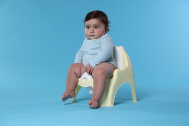 Photo of Cute little baby sitting on potty against light blue background