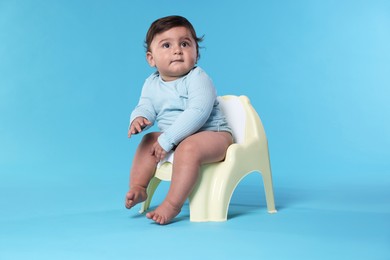 Photo of Cute little baby sitting on potty against light blue background