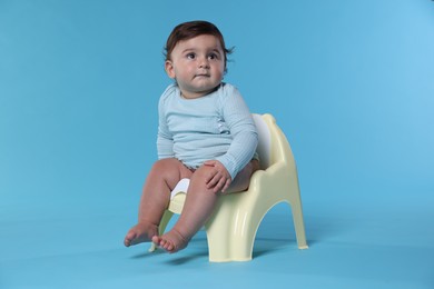 Photo of Cute little baby sitting on potty against light blue background