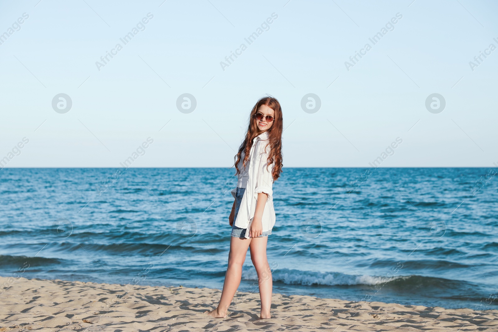 Beautiful teenage girl in sunglasses on sandy beach near sea Photo of Beautiful teenage girl in sunglasses on sandy beach near sea