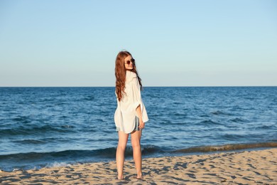 Photo of Beautiful teenage girl in sunglasses on sandy beach near sea