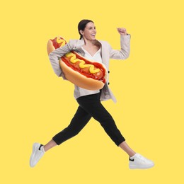 Image of Happy woman with big hot dog running against yellow background, creative collage. Fast food