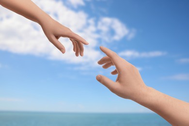 Image of Man and woman reaching to each other against seascape, closeup of hands