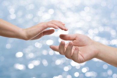 Image of Man and woman reaching to each other against sea, closeup of hands