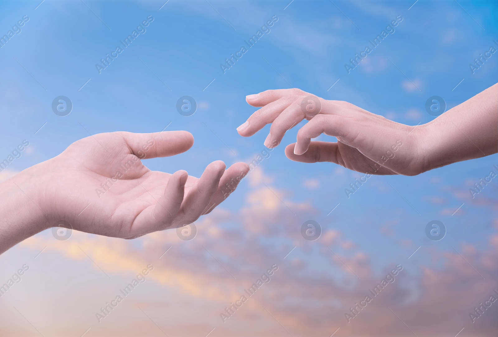 Image of Man and woman reaching to each other against sky at sunset, closeup of hands