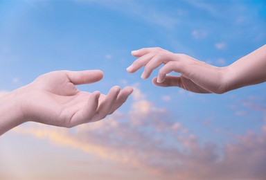 Image of Man and woman reaching to each other against sky at sunset, closeup of hands