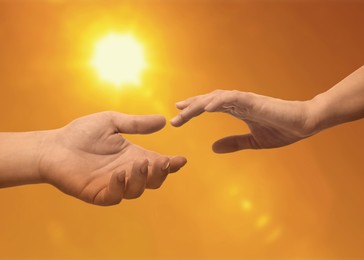 Image of Man and woman reaching to each other against sky with bright sun at sunset, closeup of hands